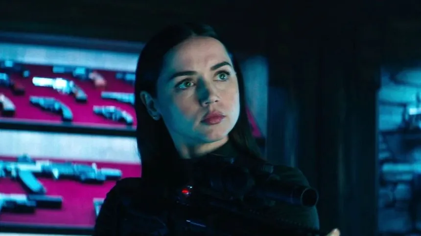 The lead character of Ballerina in tactical gear standing before pink-lit display cases of weapons