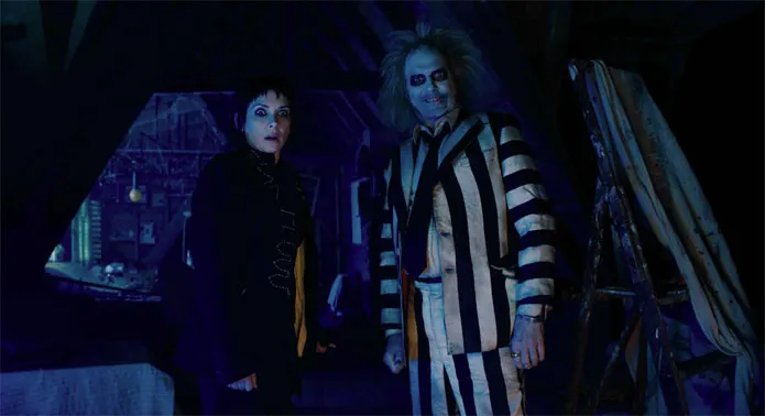 A pale-faced ghoul in a striped suit beside a dark-haired woman in a dim attic