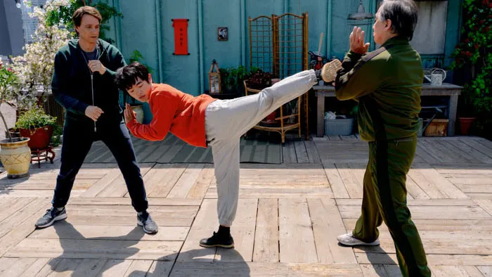 A young martial artist practicing a high kick on a city rooftop as mentors look on