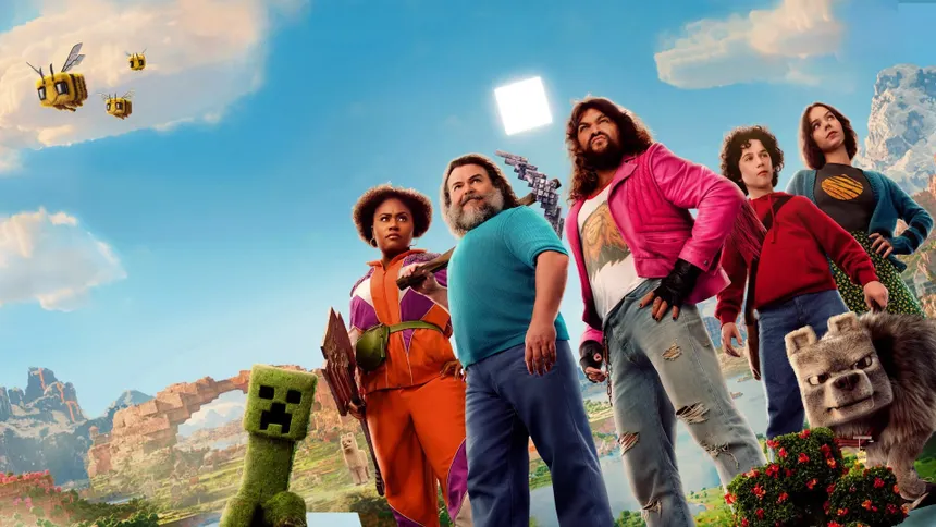 The live-action cast of A Minecraft Movie standing together beside a grass-block Creeper