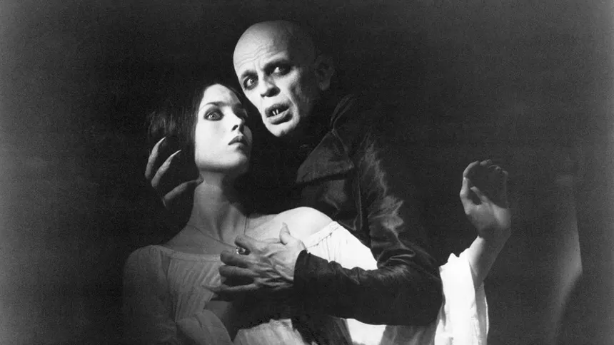 A pale, bald vampire looming over a woman in a black-and-white gothic horror still