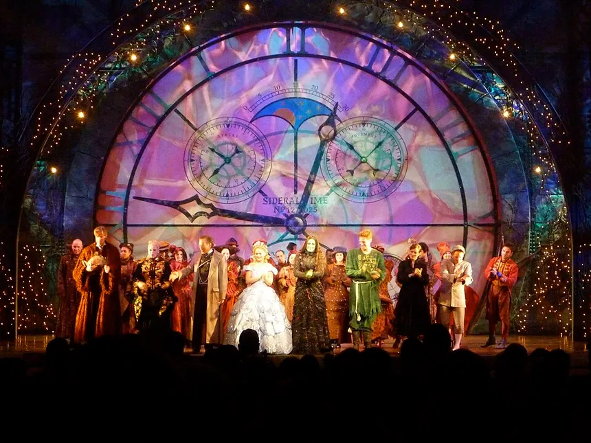 The cast of the stage musical Wicked performing before a giant clock-face backdrop